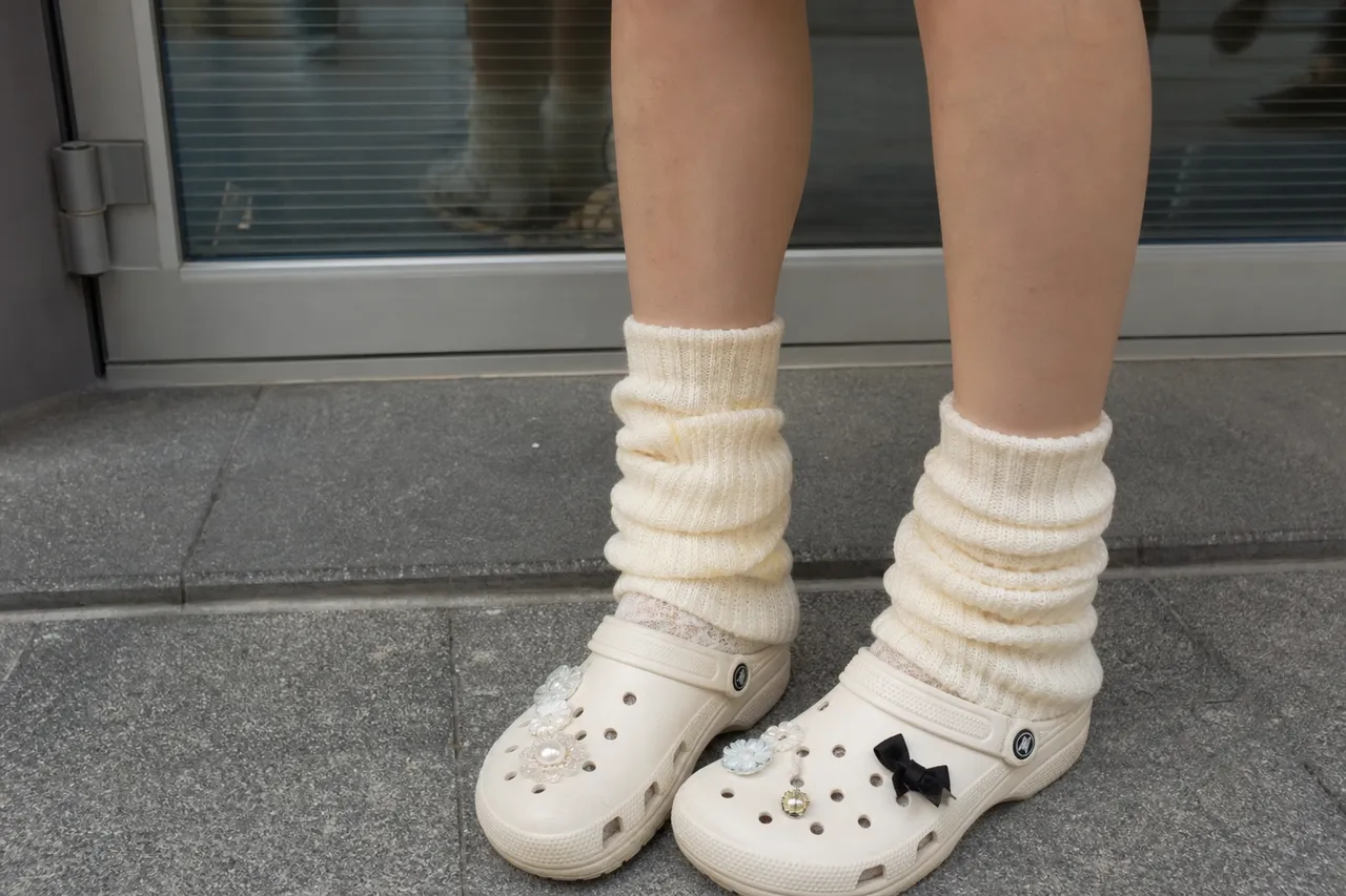 A close-up shot of a Korean woman's ankles wearing loose knit leg warmers and Crocs with lace socks, soft focus background, aesthetic fashion photography