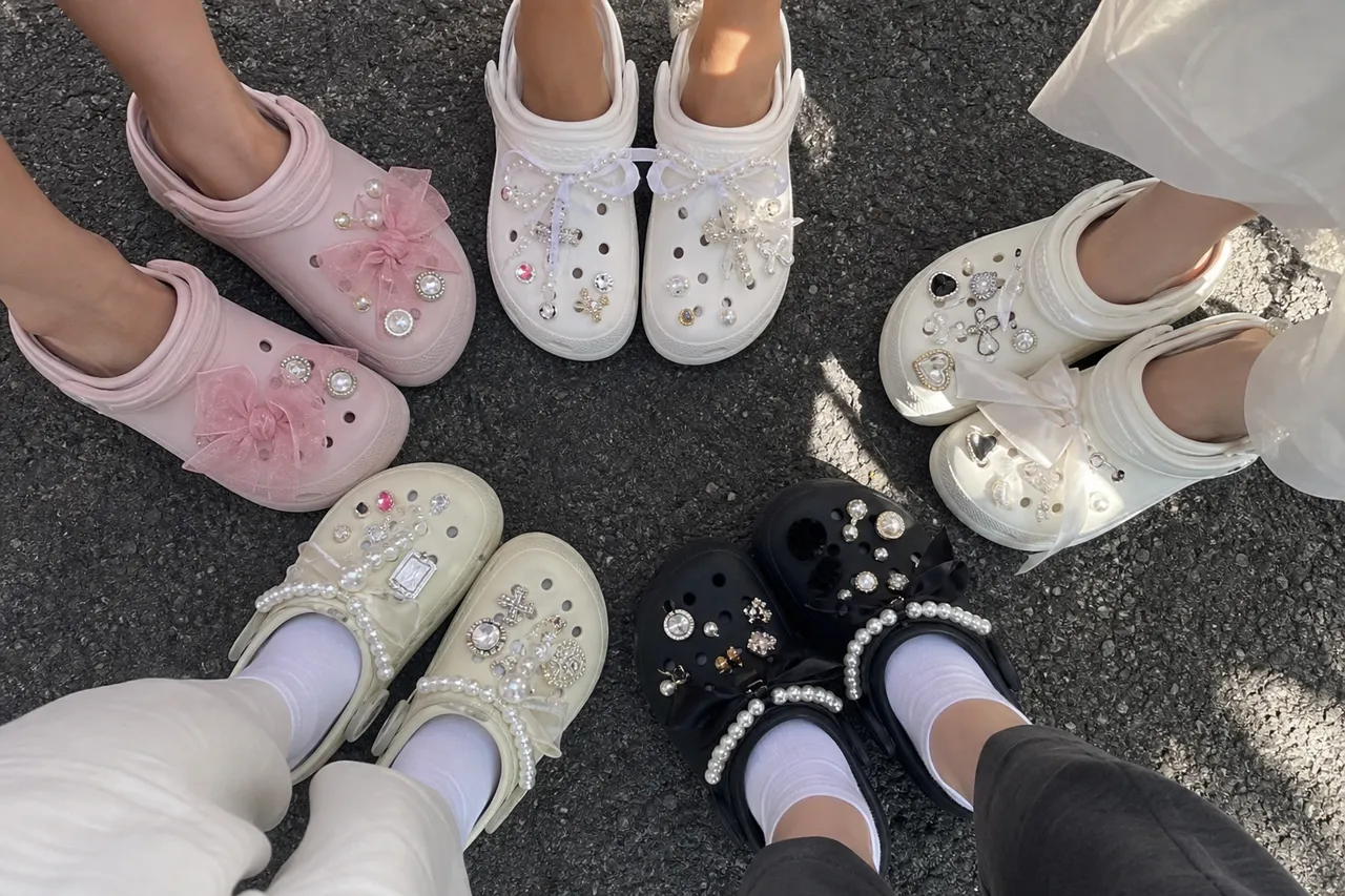 An overhead flat lay of Crocs decorated with various Jibbitz like pearls, crystals, and ribbons, colorful and artistic arrangement, bright lighting