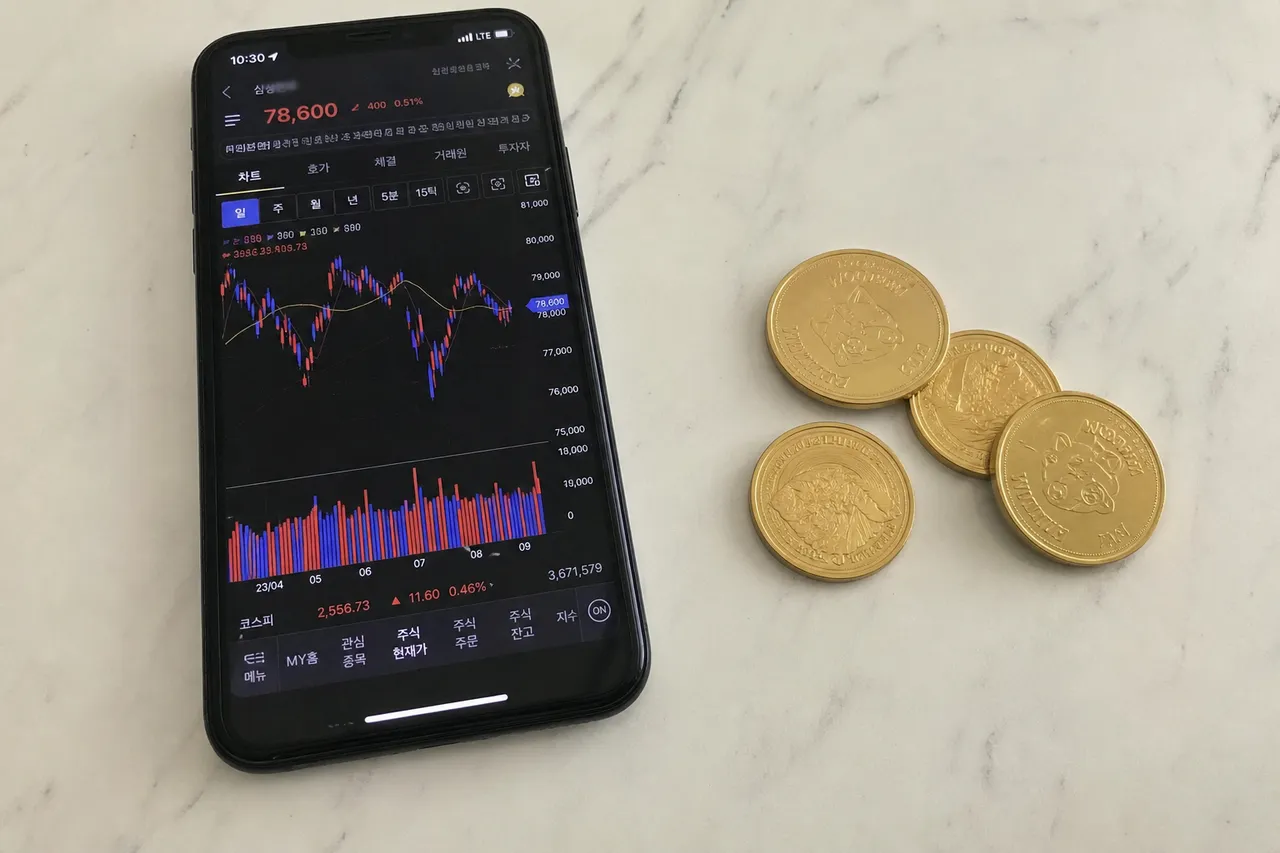 A flat lay photograph of a modern smartphone showing a stock trading app and several gold coins scattered on a white marble desk, clean minimalist aesthetic