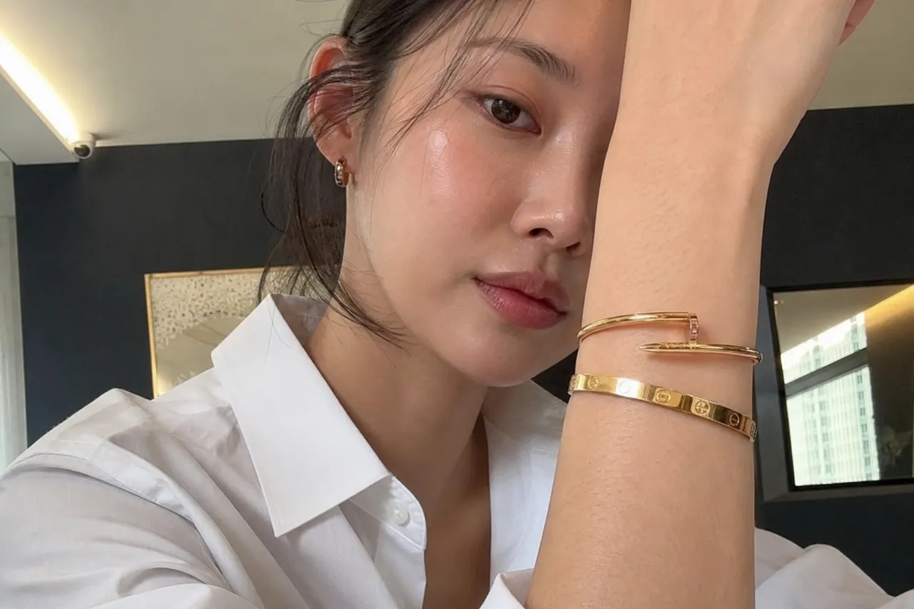A high-end fashion photograph of a Korean woman in a crisp white shirt, focusing on her wrist adorned with a gold Cartier Love bracelet and a Juste un Clou bracelet, soft natural lighting, elegant mood