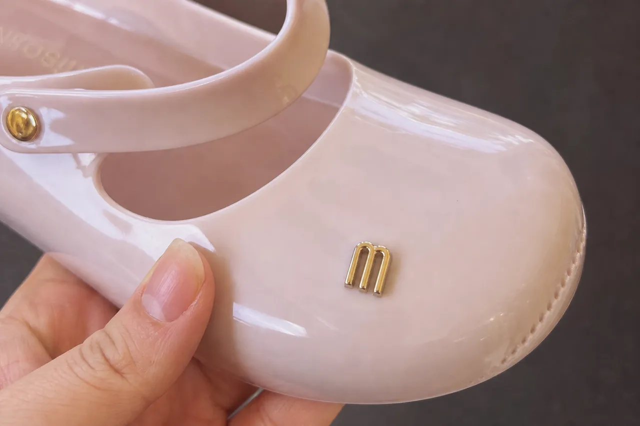 A high-resolution macro shot of the smooth texture and finish of a Melissa jelly shoe, highlighting the brand logo and material quality, bright studio lighting