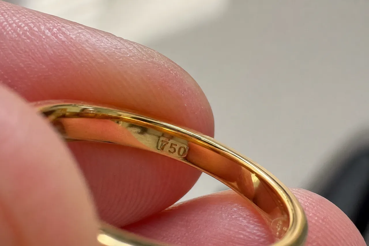 A macro close-up photograph of the inside of a gold ring showing the '750' hallmark clearly, soft natural light, shallow depth of field